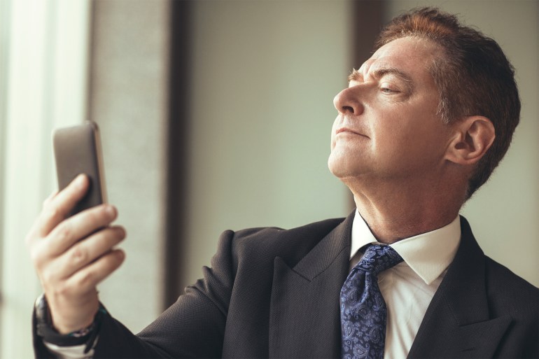 Portrait of proud senior Caucasian businessman wearing suit taking selfie with mobile phone