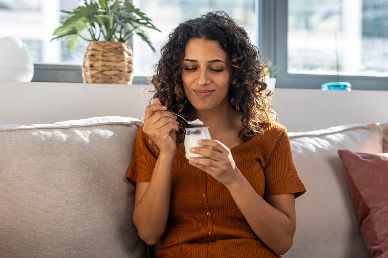 Smiling woman eating yogurt on sofa at home