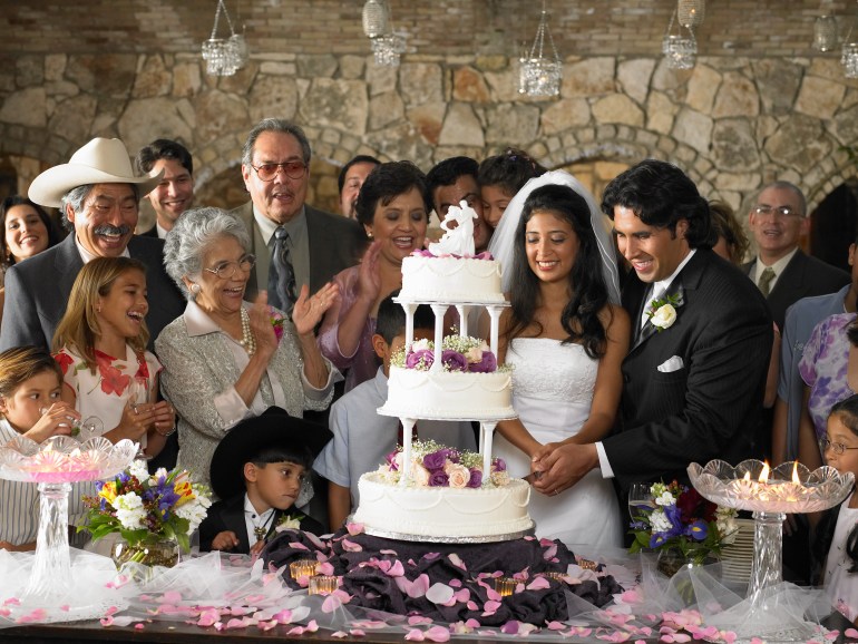 People watching bride and groom cut cake at wedding reception