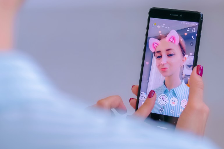 MOSCOW, RUSSIA - MAY 24, 2019: Snapchat multimedia messager with 3d face mask filter on smartphone in woman hands at home. Face detection, AR, beauty, selfie, vogue, fashion, trendy concept