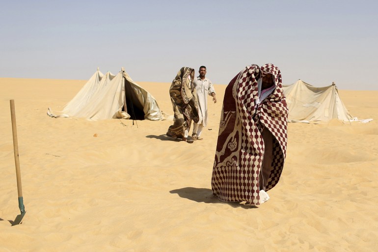 A worker helps patients, who are wrappd in a blanket, leave a "sauna" tent after their sand baths in Siwa, Egypt, August 12, 2015. In the searing heat of summer in western Egypt, at the hottest time of the day, sufferers of rheumatism, joint pain, infertility or impotence lie buried neck-deep in the sand of Siwa near Dakrour Mountain. Locals say taking a sand bath is a natural therapy with powers to cure many medical conditions. Patients relax in the shade before treatment, which includes massages by the feet of health workers after they submerge their patients up to their neck in the desert. Patients drink mint tea in tents following the treatment. REUTERS/Asmaa Waguih PICTURE 19 OF 24 FOR WIDER IMAGE STORY "THE HOT SAND BATHS OF SIWA". SEARCH "ASMAA SIWA" FOR ALL IMAGES