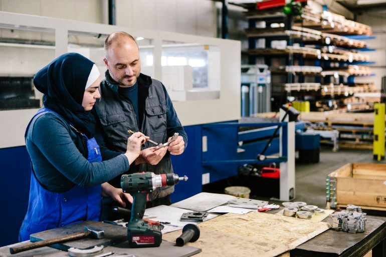 technician explains a work tool to a female trainee in a workshop