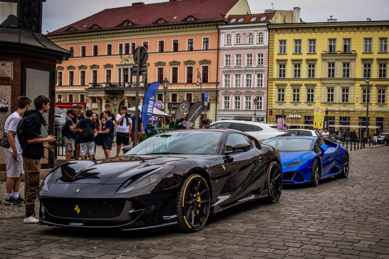 Wroclaw, Poland, July 28, 2024. Luxury cars, a black Ferrari and a blue Lamborghini, parked in a square in Wroclaw. Young people are observing and taking photos, amazed by the beauty of these cars. شترستوك