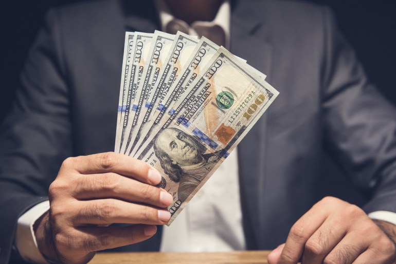 Businessman showing US dollar bills at the table in dark background - making money, bribery and venality concepts