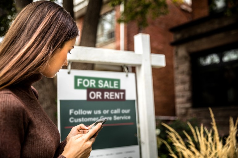 Woman photographing a real estate sign for a nice house for sale in downtown.