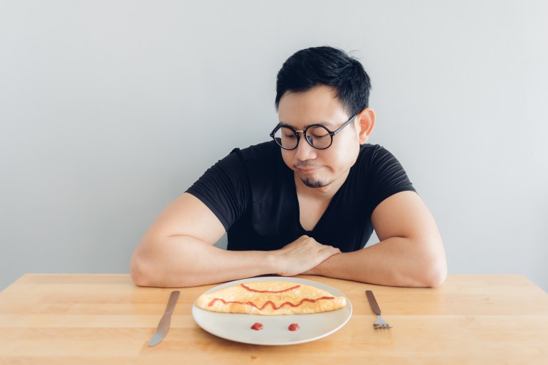 Sad and boring Asian man is eating homemade breakfast set of omelet.