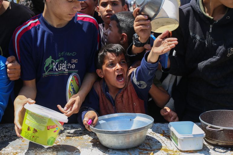A Palestinian boy gestures as he waits for a portion of hot food distributed by a charity kitchen at the Nuseirat refugee camp in the central Gaza Strip on May 5, 2025.