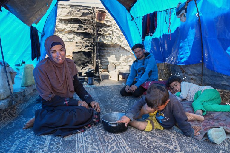 Ward Nar, left, reacts as she speaks with the photographer after returning empty-handed from attempting to receive donated food for her family, including her husband Mohammed Zaharna (center right) and their children, Sally (right) and Raed, at a community kitchen in Khan Younis, in the southern Gaza Strip, Friday, May 9, 2025. (AP Photo/Abdel Kareem Hana)
