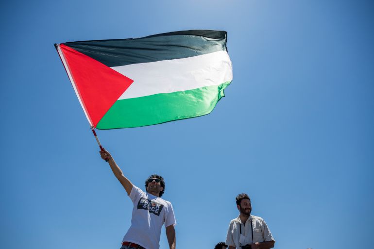 CATANIA, ITALY - JUNE 01: A young activist raises the Palestinian flag as the Madleen sets sail for Gaza on June 01, 2025 in Catania, Italy. Swedish activist Greta Thunberg is among those who will attempt to sail to Gaza on a boat organized by the Freedom Flotilla Coalition (FFC), in a bid to break Israel's blockade of the Palestinian territory. Freedom Flotilla had to abort a previous journey in early May after it said its boat came under attack by drones in international waters near Malta. (Photo by Fabrizio Villa/Getty Images)